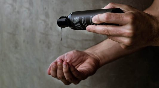 Close-up of hands pouring a black bottle's contents, showcasing minimalist packaging and highlighting trends in sleek, modern beauty product design