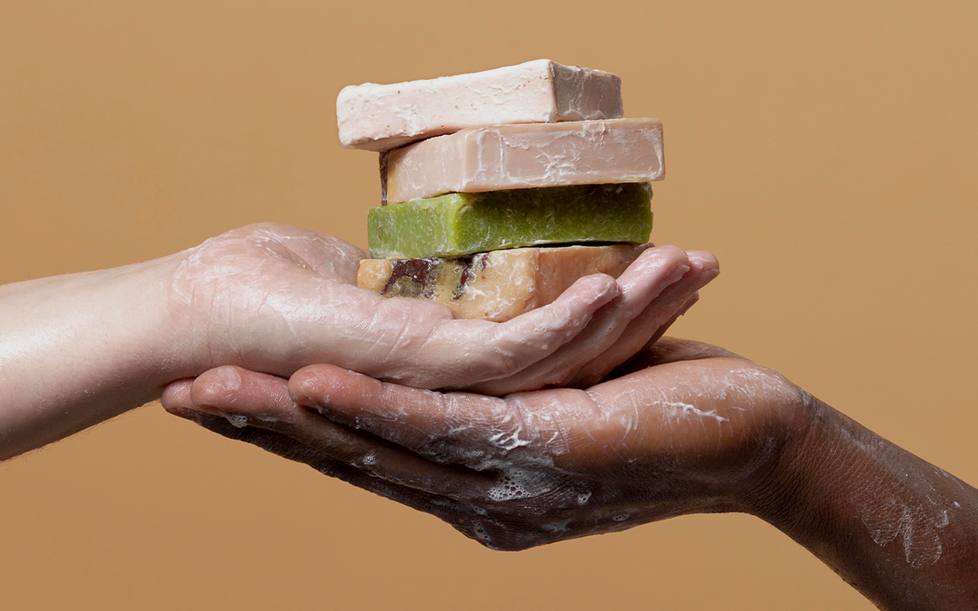 Two soapy hands holding a stack of colorful handmade soaps, symbolizing sustainability and natural skincare in private label body care products