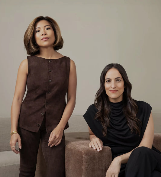 Two women entrepreneurs posing confidently indoors, one standing and one seated.