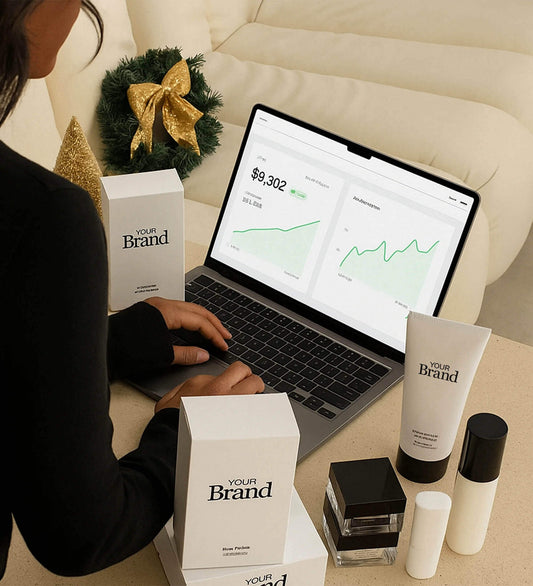 Person reviewing sales analytics on a laptop surrounded by ‘Your Brand’ skincare products and holiday decorations.