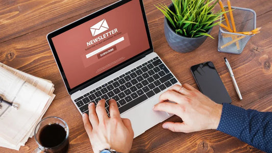 Person typing on a laptop with a "Newsletter Subscribe" screen, set on a wooden desk alongside a phone, coffee, and greenery—ideal for promoting email marketing strategies