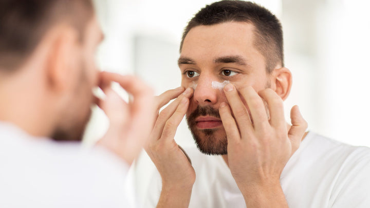 A male applying under eye cream, depicting the current shift in men's skincare going from only using bar soaps to now serums, creams, facials, etc. 