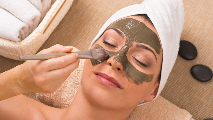 Woman relaxing during a spa treatment with a brush applying a marine-based facial mask, highlighting the growing trend in ocean-inspired beauty products