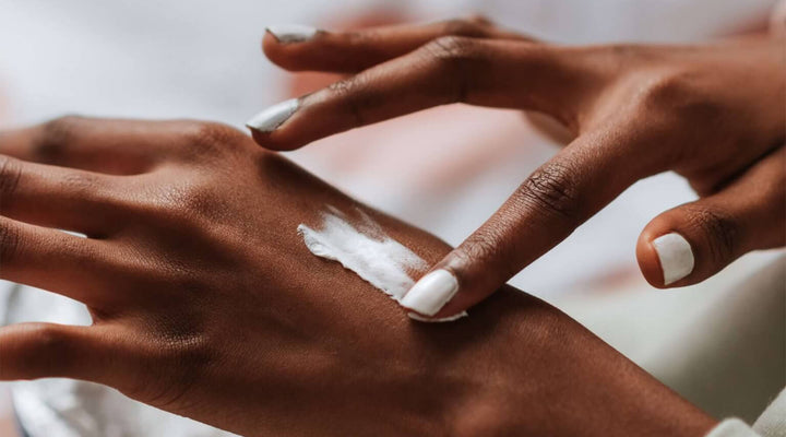 Close-up of hands applying a white cream on the back of one hand, showcasing smooth skin and a focus on skincare