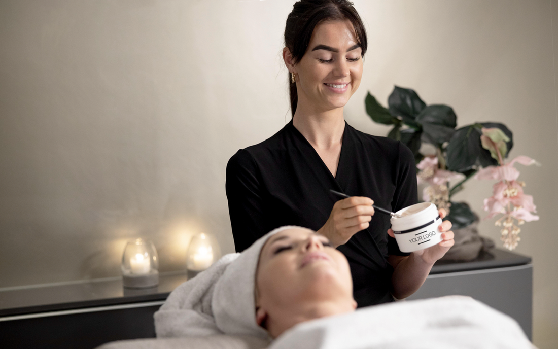 A medspa technician applying a mask on a woman's face lying down on the practitioner's bed with candles around