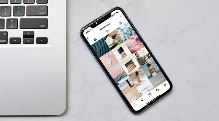 Smartphone displaying a curated Instagram grid beside a laptop on a marble surface, emphasizing the importance of finding a cohesive social media brand voice