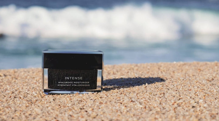 Luxury skincare jar labeled "Intense Hyaluronic Moisturizer" placed on sandy beach with ocean waves in the background, symbolizing hydration and premium beauty branding