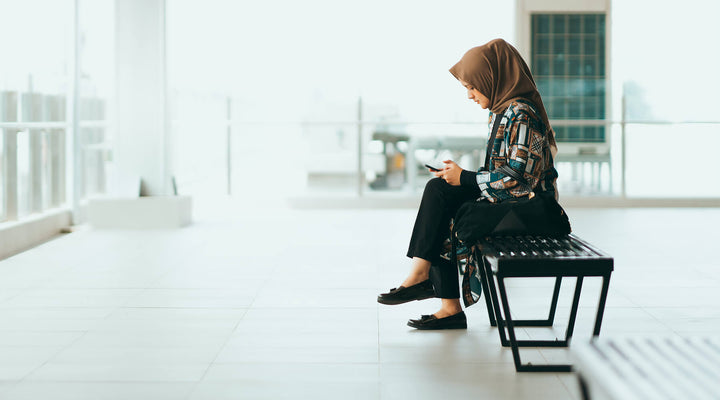 Side profile of a woman sitting on a bench, focused on her phone in a bright, minimalist setting, symbolizing goal-setting and intentional planning