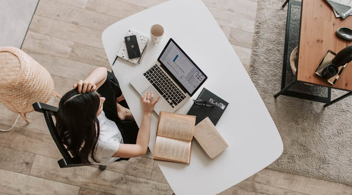 Overhead view of a woman working on a laptop at a desk surrounded by books and packaging, highlighting the role of customer reviews and content in driving SEO success