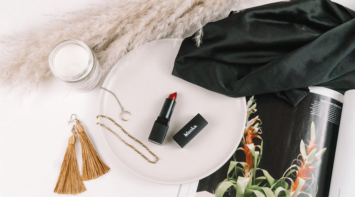 Flat lay of a Blanka red lipstick surrounded by stylish accessories, including gold jewelry, a candle, and soft fabrics, perfect for showcasing luxury and elegance in beauty branding