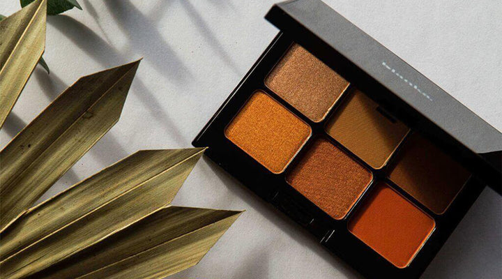 A warm-toned makeup palette displayed with natural light and golden leaves, symbolizing elegance and creativity in beauty branding