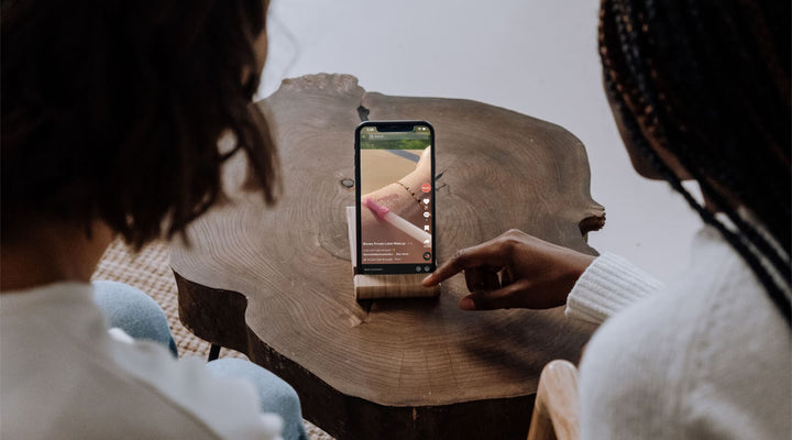  Two women watching a TikTok video featuring a beauty product on a phone resting on a wooden table, highlighting the power of social media marketing for brand promotion