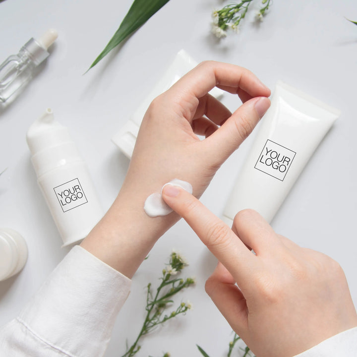 Woman applies moisturizer to her hand, with bottles of private label-ready products in the background that can feature your logo on them