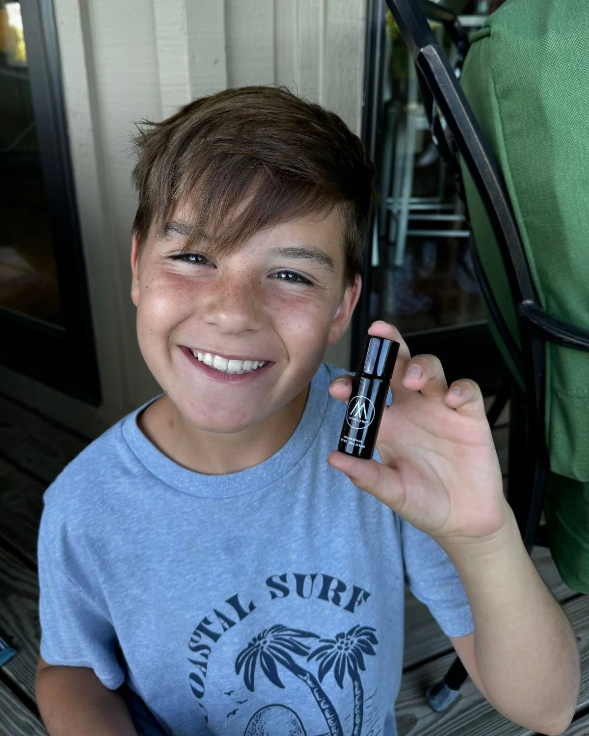 Child holding a small black bottle with a cap, wearing a blue 'Coastal Surf' t-shirt.