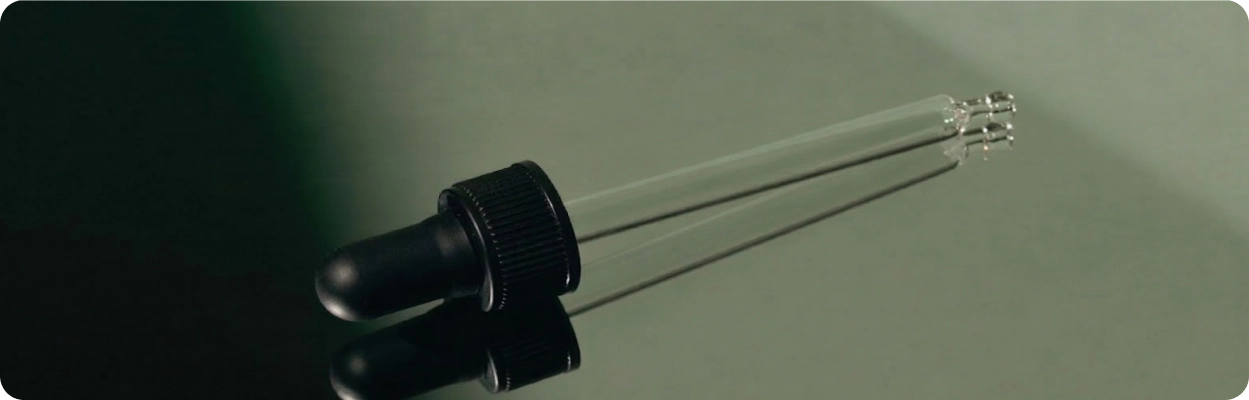 Black dropper bottle with a clear pipette on a reflective surface