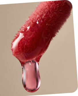 Close-up of a red cosmetic applicator with a drop of liquid on a beige background
