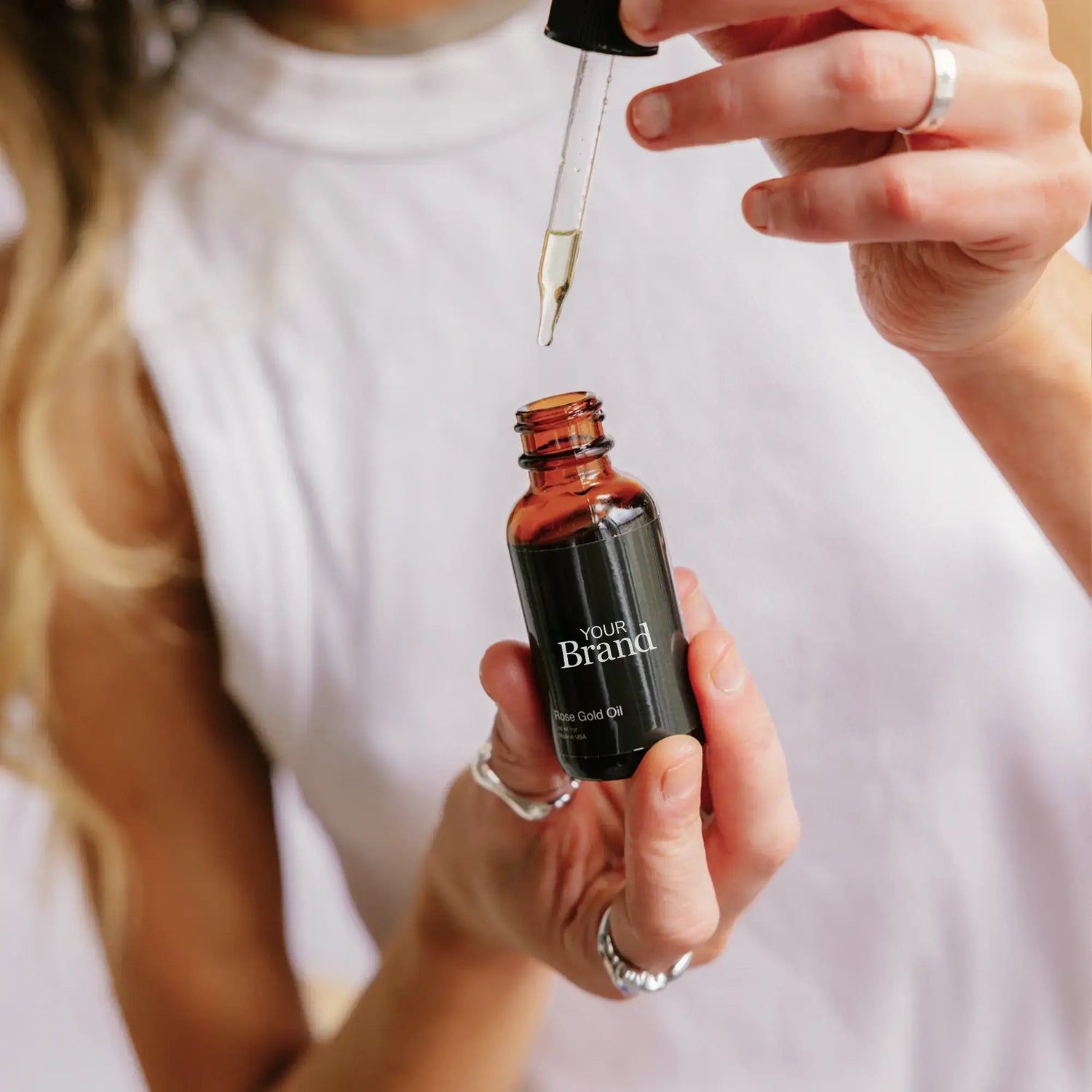 Person holding a dropper over a small brown serum bottle with a white shirt