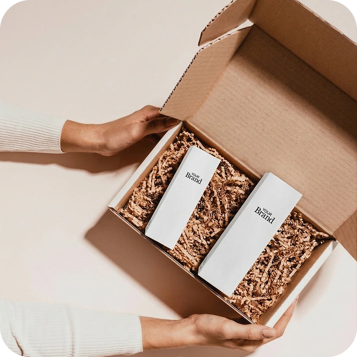 Person opening a cardboard box containing two white boxes with 'The Brand' logo.