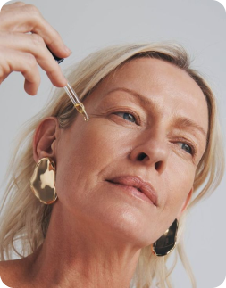 Person applying a dropper of liquid to their face against a neutral background