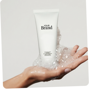 Hand holding a tube of cream with visible brand text on a light gray background