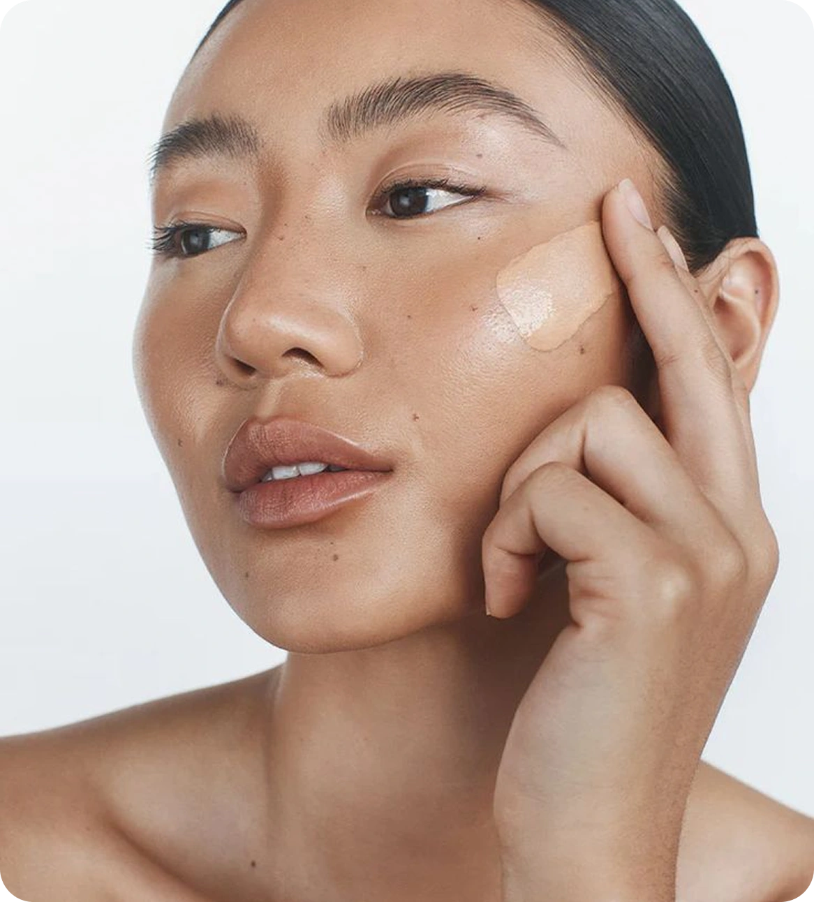 Woman applying concealer from custom branded bottle on her cheek