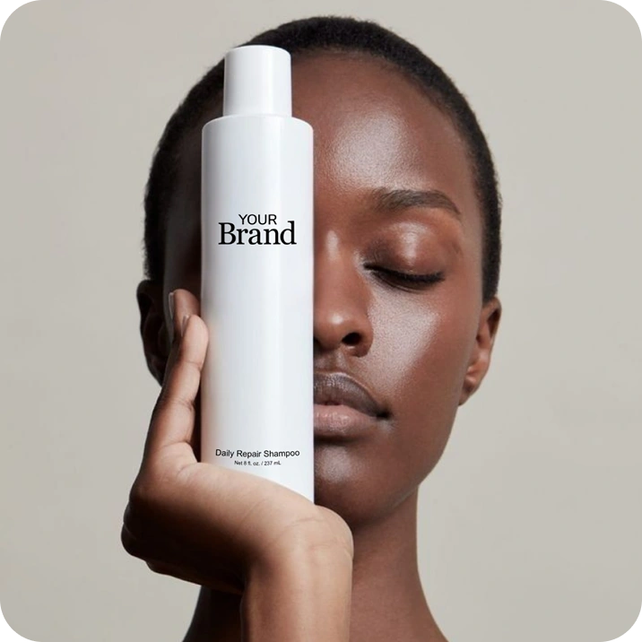 Person holding a white shampoo bottle labeled 'Your Brand' against a neutral background