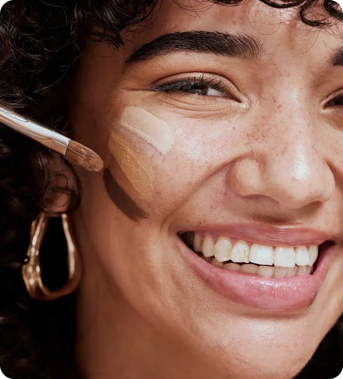 Close-up of a woman's face with makeup application, wearing gold hoop earrings.