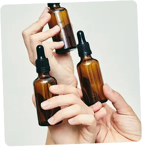 Three brown glass dropper bottles held by hands against a light background