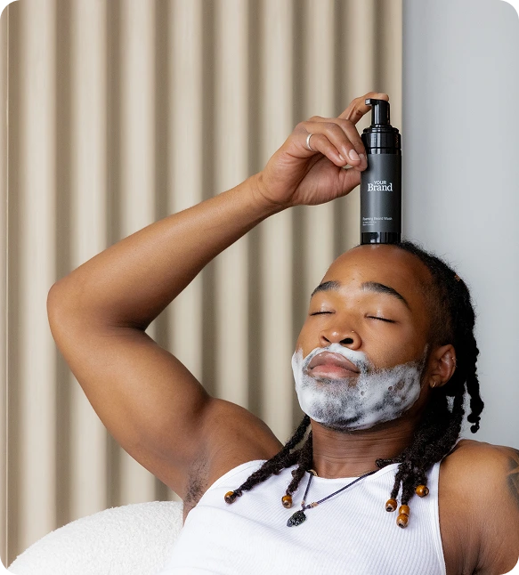 Man with a beard holding a bottle of hair product against a neutral background