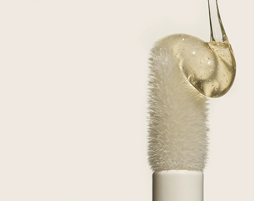 Makeup brush with a droplet of liquid on a beige background