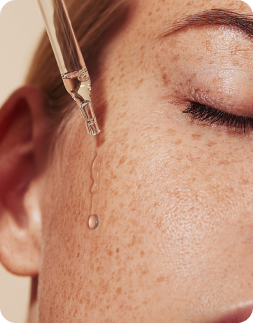 Close-up of a dropper applying a drop of liquid to a person's skin.